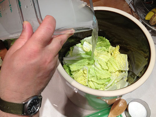 brine being poured over nappa cabbage leaves in a fermentation crock